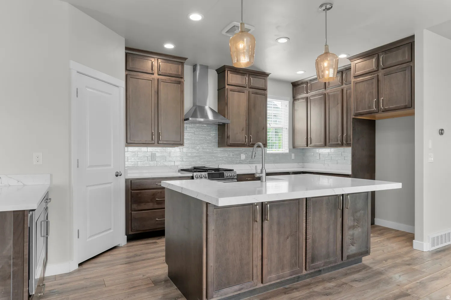 Kitchen featuring wood-finish flooring, wood cabinetry, white countertops, tile backsplash, and a stainless steel range hood