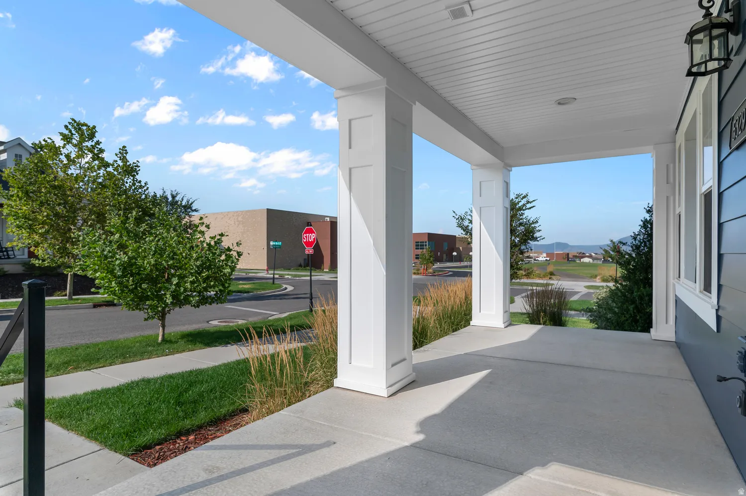 Covered concrete porch with white support columns, exterior wall lantern, and horizontal siding