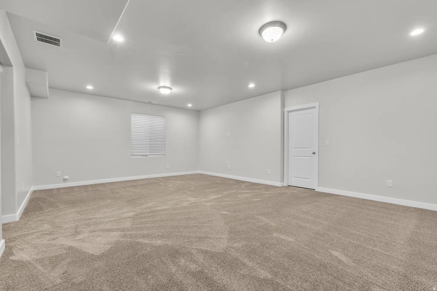 Expansive room with neutral carpeting, recessed lighting, and a white paneled door