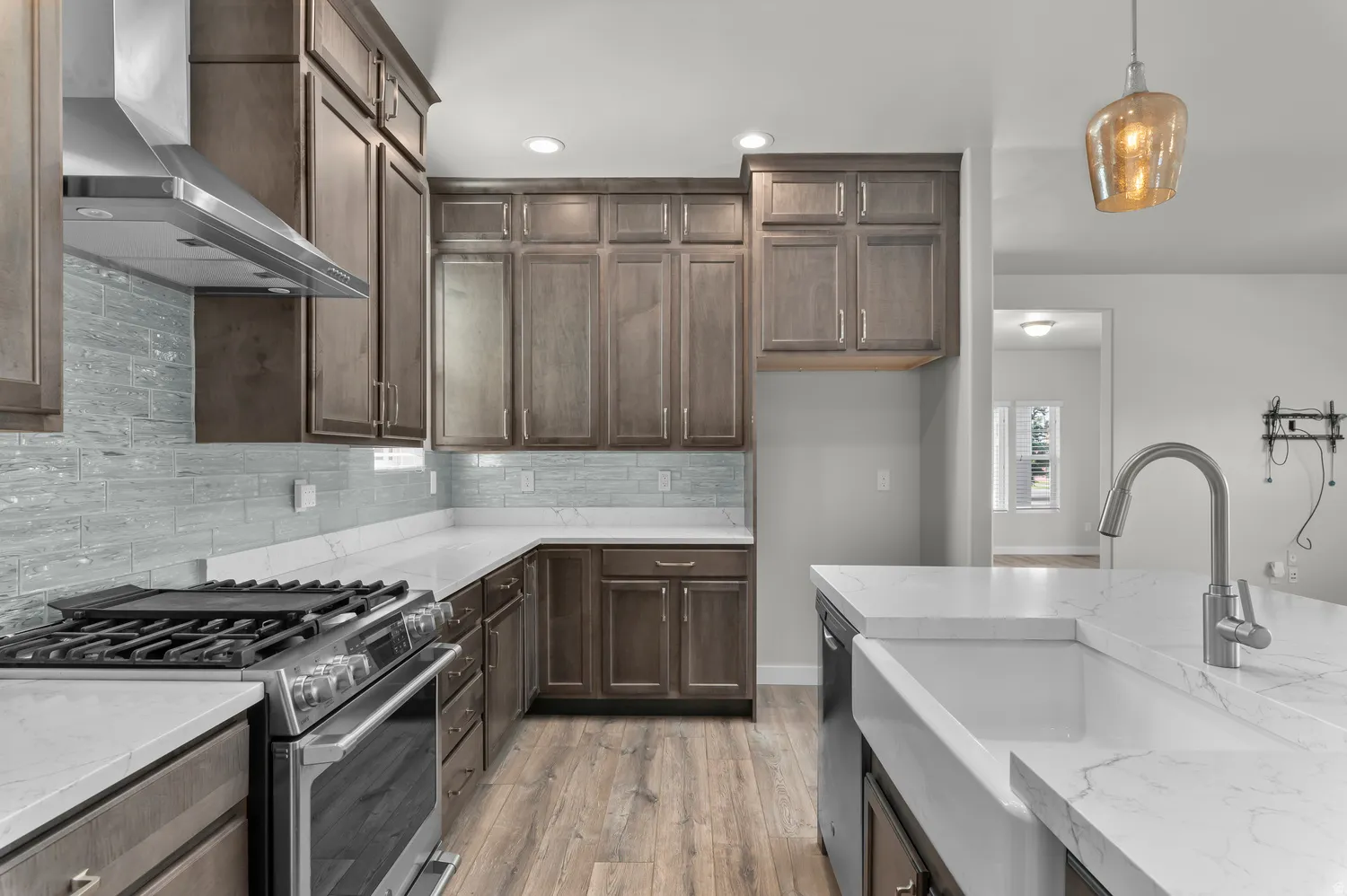 Chef's kitchen featuring a stainless steel range with griddle, farmhouse sink, quartz countertops, and wood-finish flooring