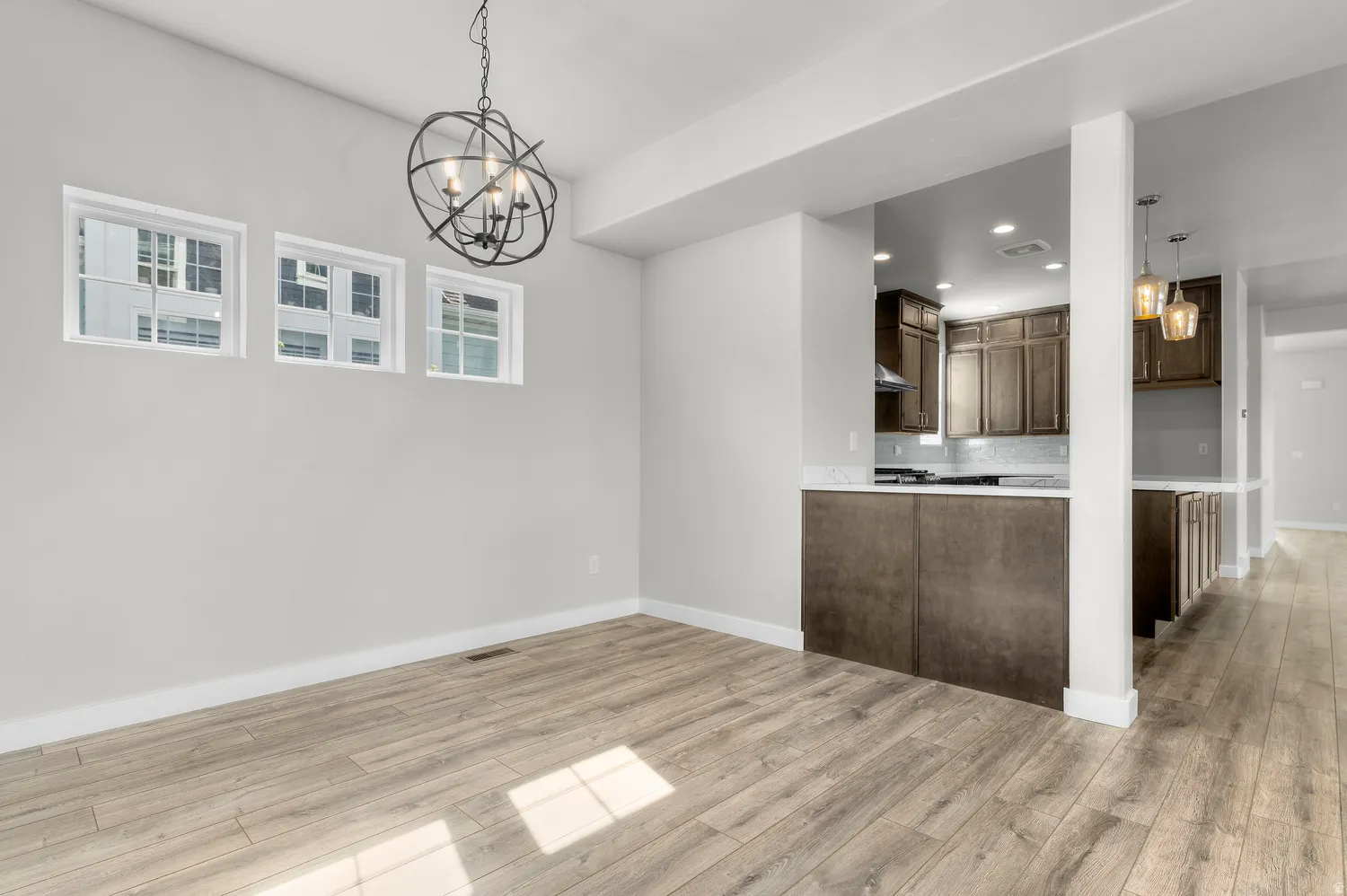 Open-concept living space with wood-finish flooring, a contemporary chandelier, and three transom windows