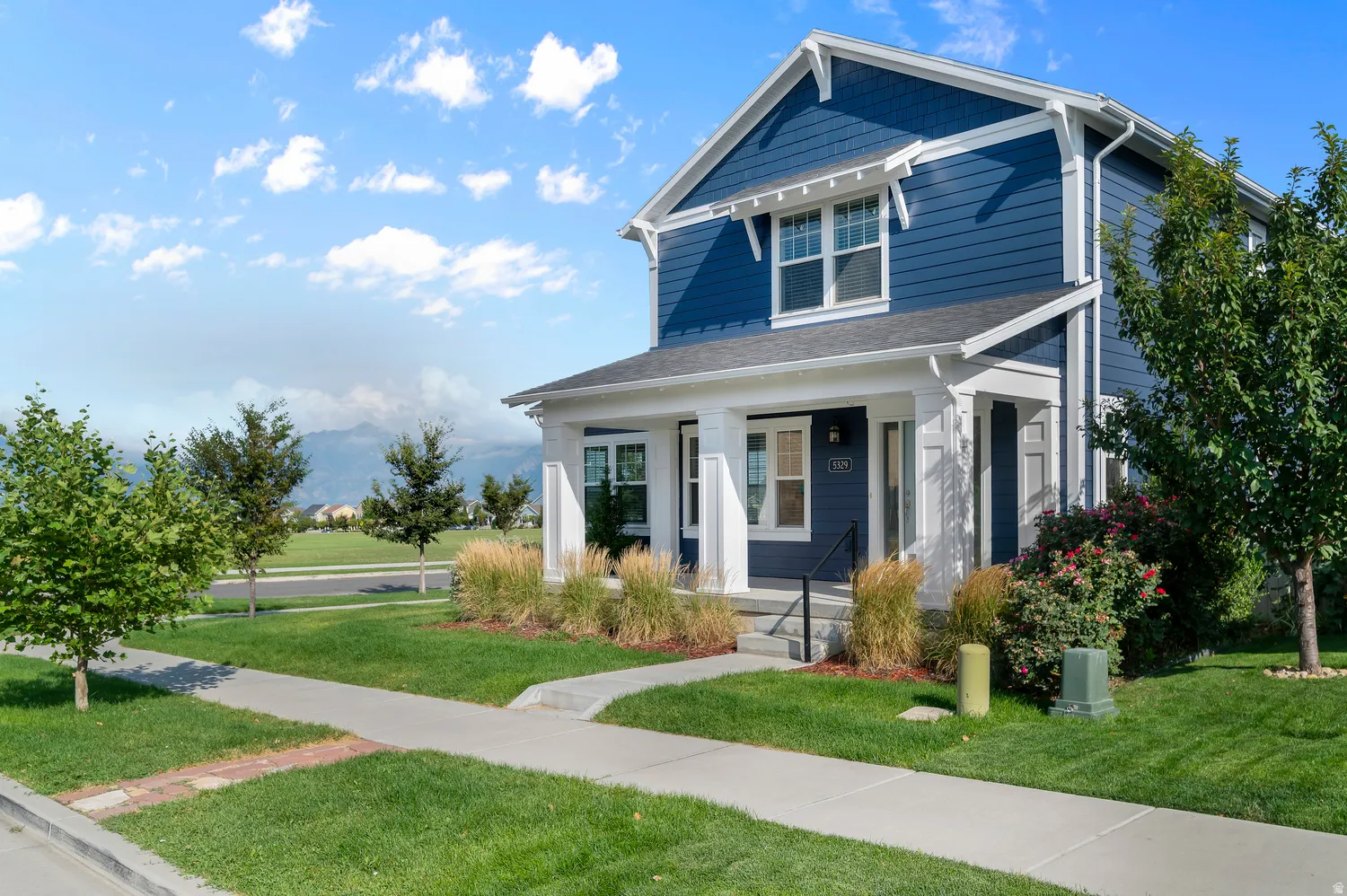 Exterior featuring blue siding, white trim, a covered porch, and well-maintained landscaping with mature trees