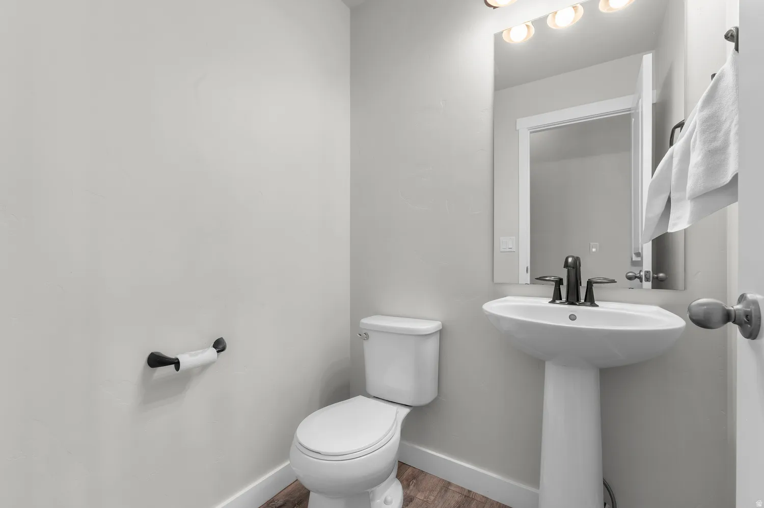 Pedestal sink with dark-toned fixtures, rectangular mirror, and wood-finish flooring