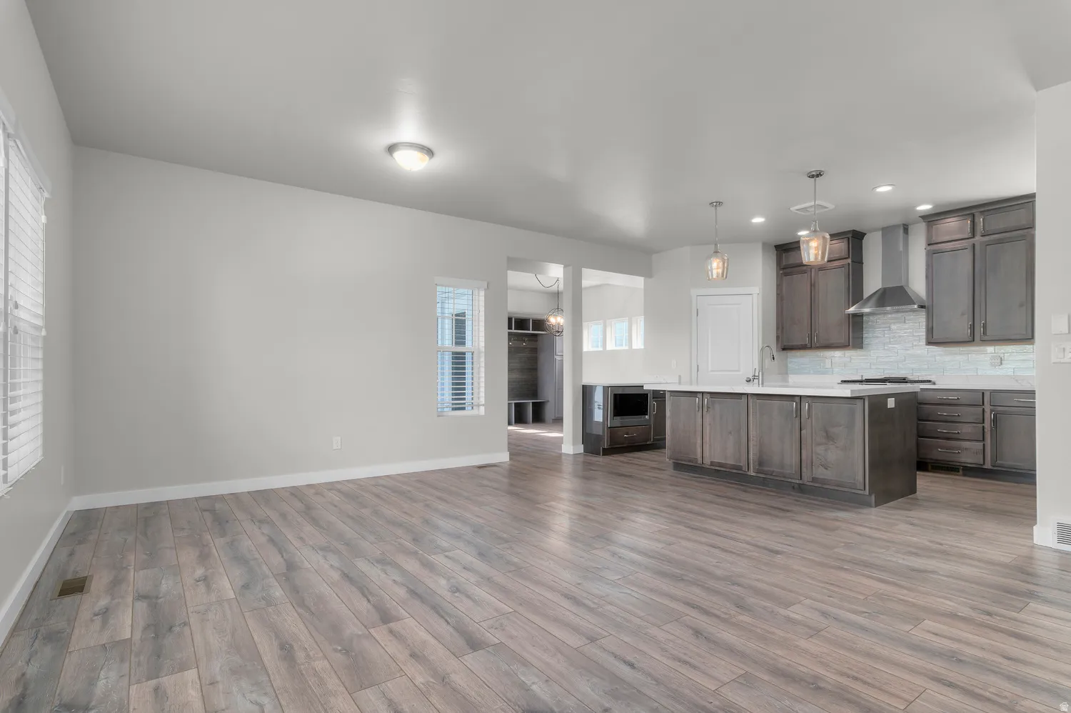 Wood-finish flooring, recessed lighting, kitchen island with built-in cabinetry, stainless steel range hood, and subway tile backsplash