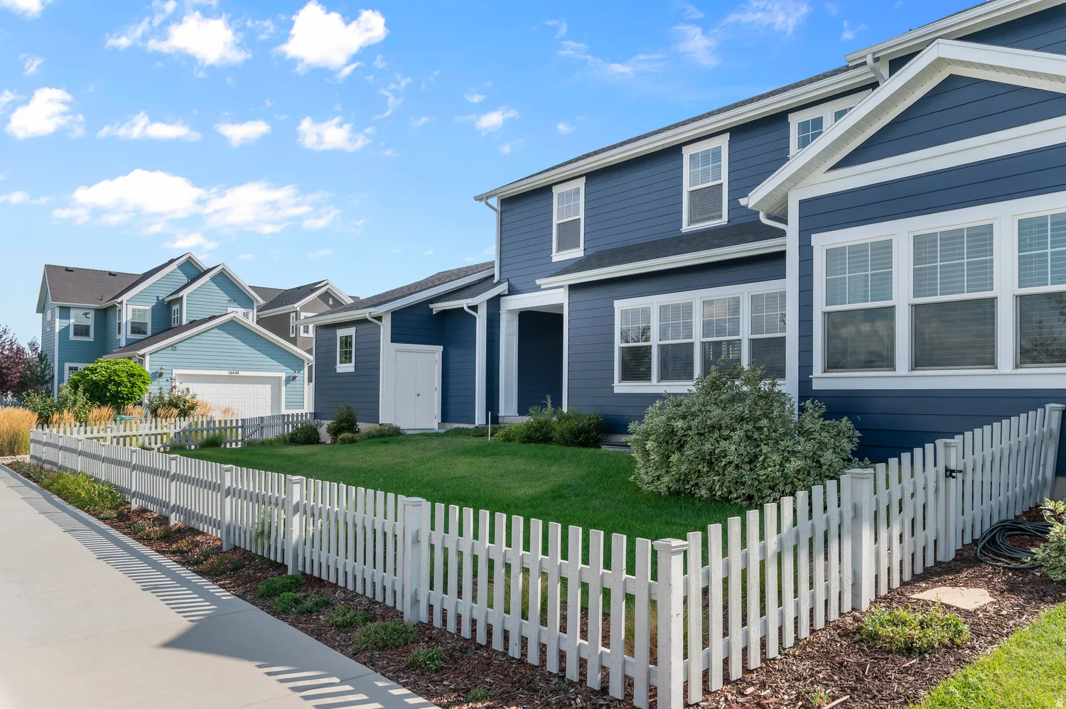 Blue horizontal siding, white trim, white-framed windows, white picket fence, and a green lawn