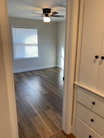 Room featuring wood-finish flooring, a window with horizontal blinds, and a ceiling fan with integrated lighting