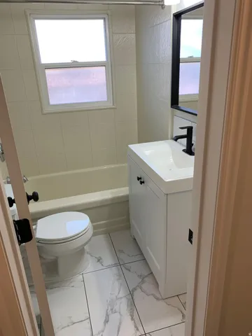 White vanity with black hardware, modern black faucet, white rectangular sink, framed mirror, and white tile flooring