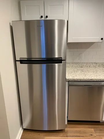 Stainless steel refrigerator, stainless steel dishwasher, white shaker-style cabinetry, subway tile backsplash, and wood-finish flooring