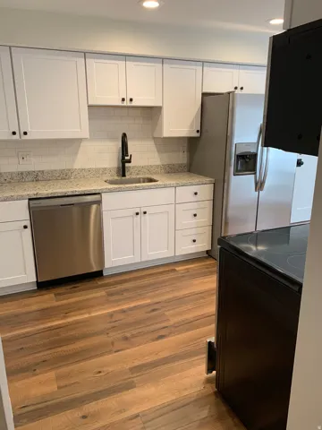 Kitchen featuring white shaker cabinetry, speckled countertops, a subway tile backsplash, stainless steel appliances, and wood-finish flooring