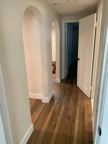 Hallway featuring multiple arched doorways, wood-finish flooring, white baseboards, and a white recessed light fixture
