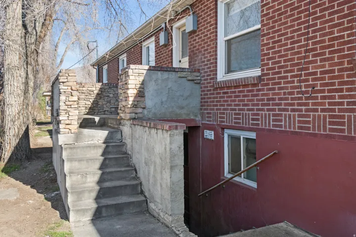 Brick exterior with decorative band, stone-clad retaining walls, concrete stairs, and a lower-level window