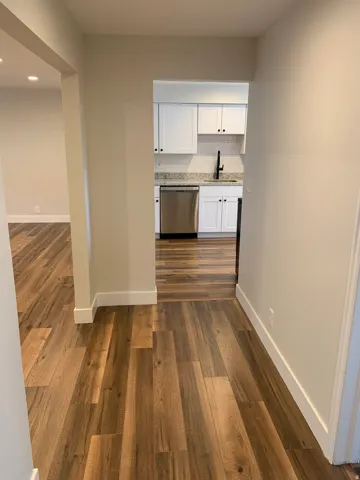 Wood-finish flooring throughout, recessed lighting, white cabinetry, stainless steel dishwasher, and a black gooseneck faucet