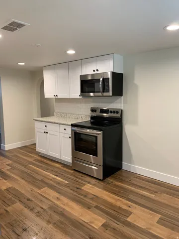 White shaker-style cabinetry, stainless steel appliances, speckled countertops, subway tile backsplash, and wood-finish flooring