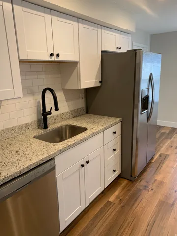 Updated kitchen featuring white shaker cabinetry, granite countertops, a stainless steel sink with a matte black faucet, and wood-finish flooring