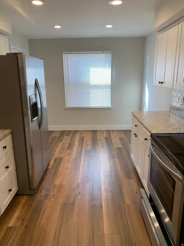 Recessed lighting, wood-finish flooring, white cabinetry with dark hardware, stainless steel appliances, and light-toned countertops