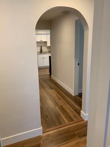 Archway entry to the kitchen featuring wood-finish flooring, white cabinetry, and granite-style countertops