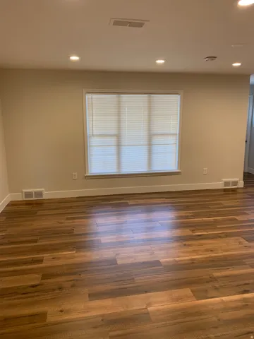 Recessed ceiling lighting, wood-finish flooring, and a large window with blinds