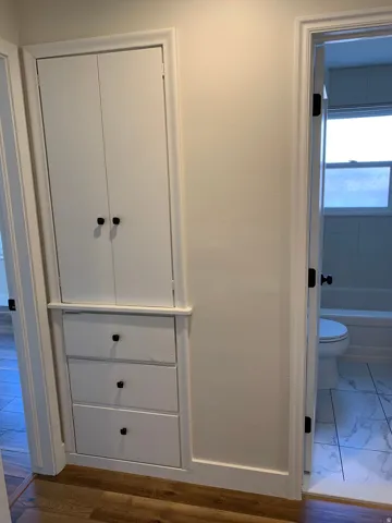 Built-in white cabinetry with matte black hardware, three lower drawers, and wood-finish flooring