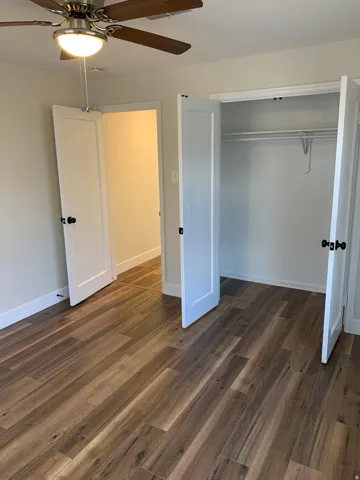 Wood-finish flooring, ceiling fan with integrated lighting, white interior doors, and built-in closet with hanging rod