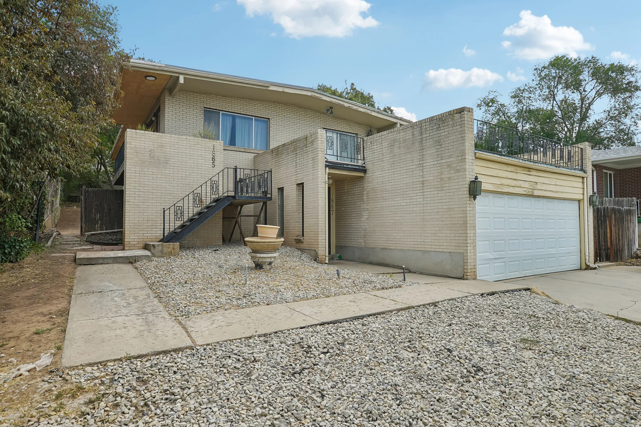 Brick exterior with a two-car garage, wrought iron staircase, and a low-maintenance gravel and concrete front yard