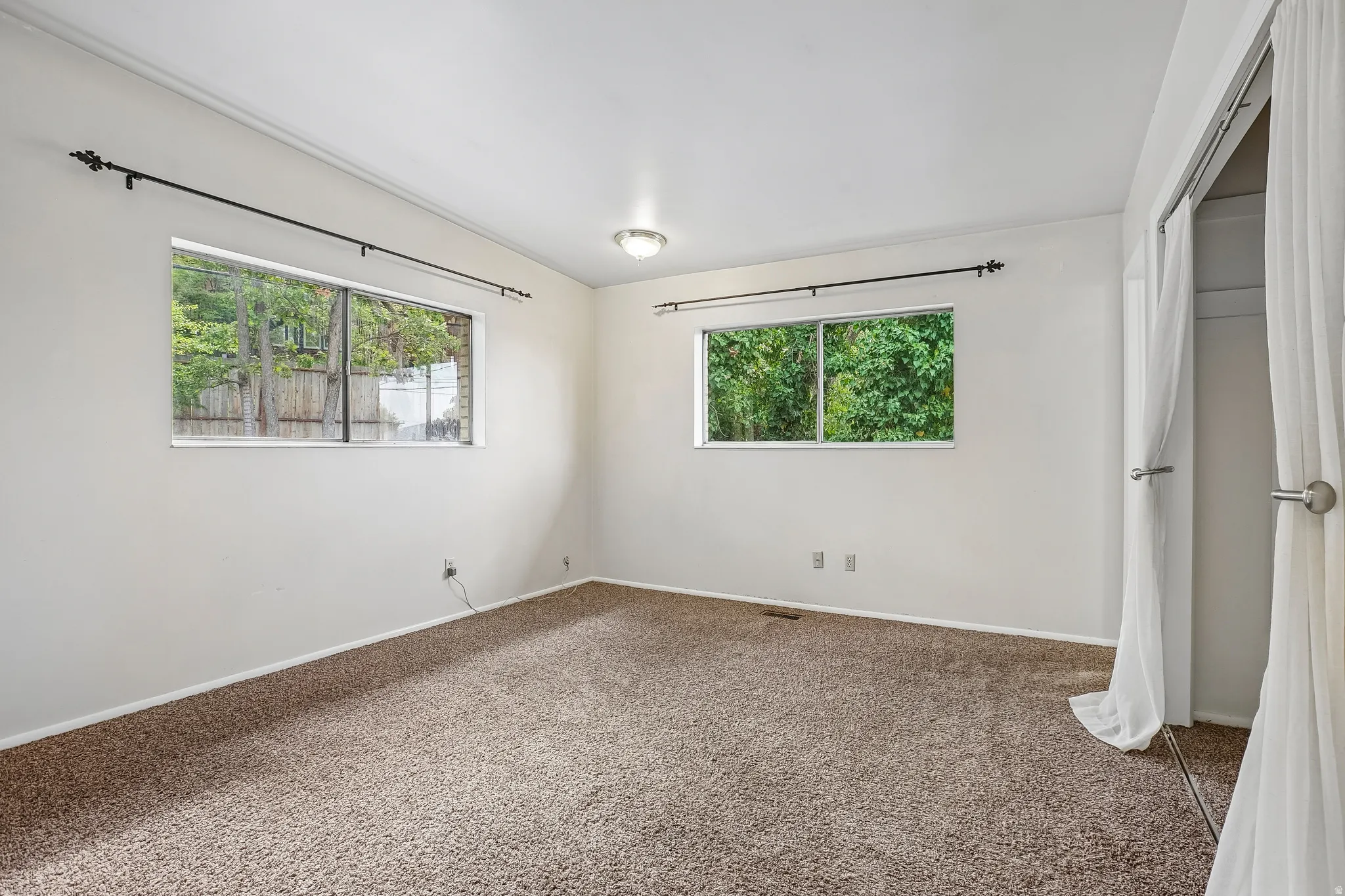 Neutral-toned carpet flooring, white walls, two large windows, and a built-in closet with sliding doors