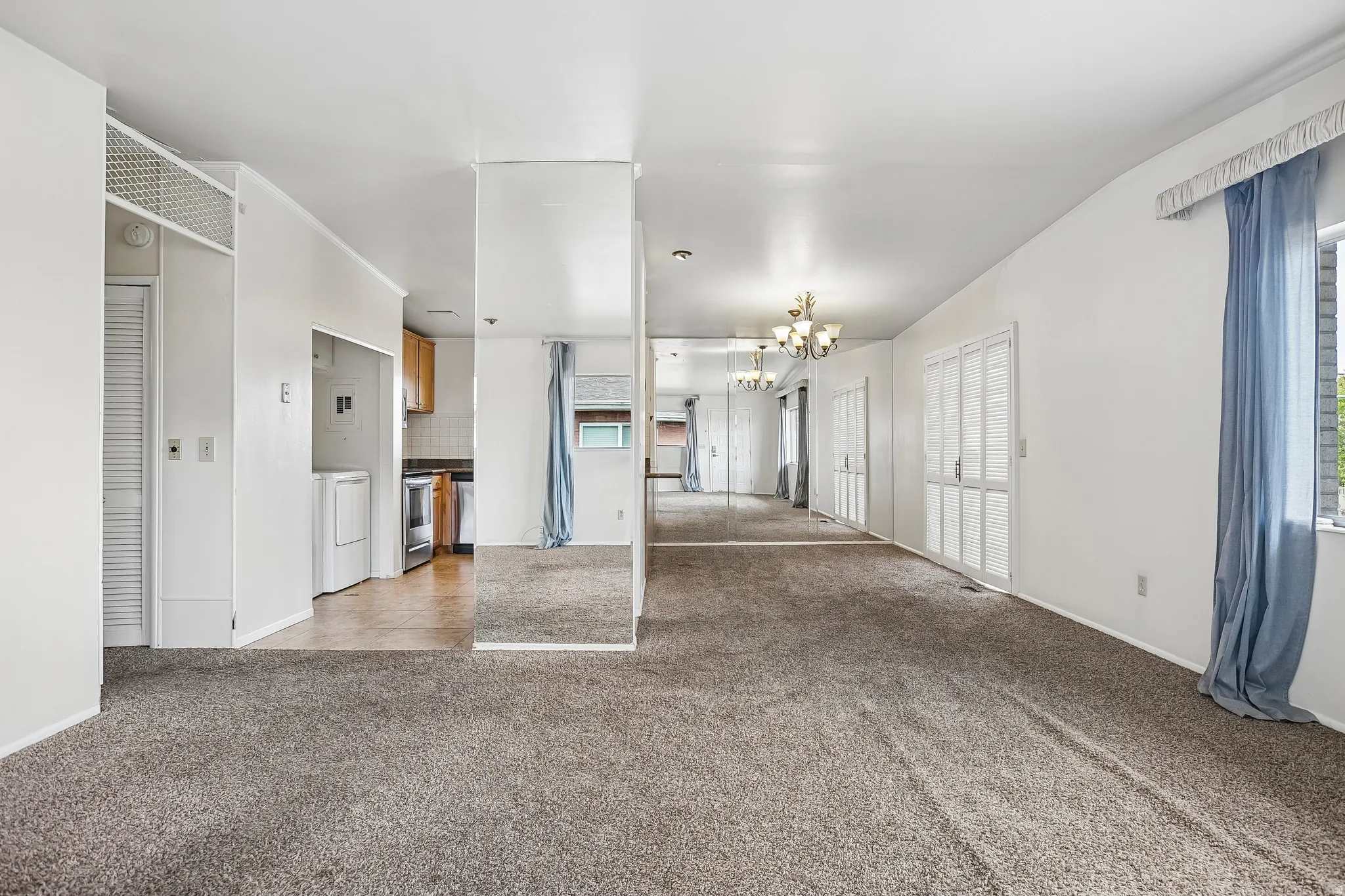 Spacious living area with wall-to-wall carpeting, mirrored accent walls, and a multi-light chandelier
