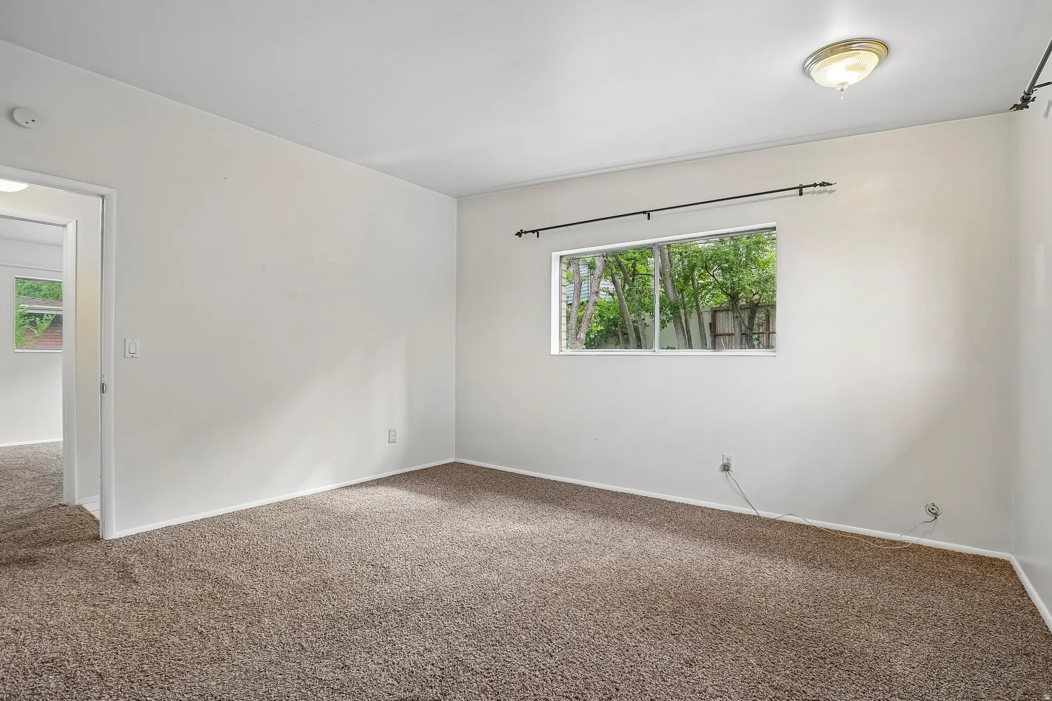 Wall-to-wall carpeting and a single window with a black curtain rod