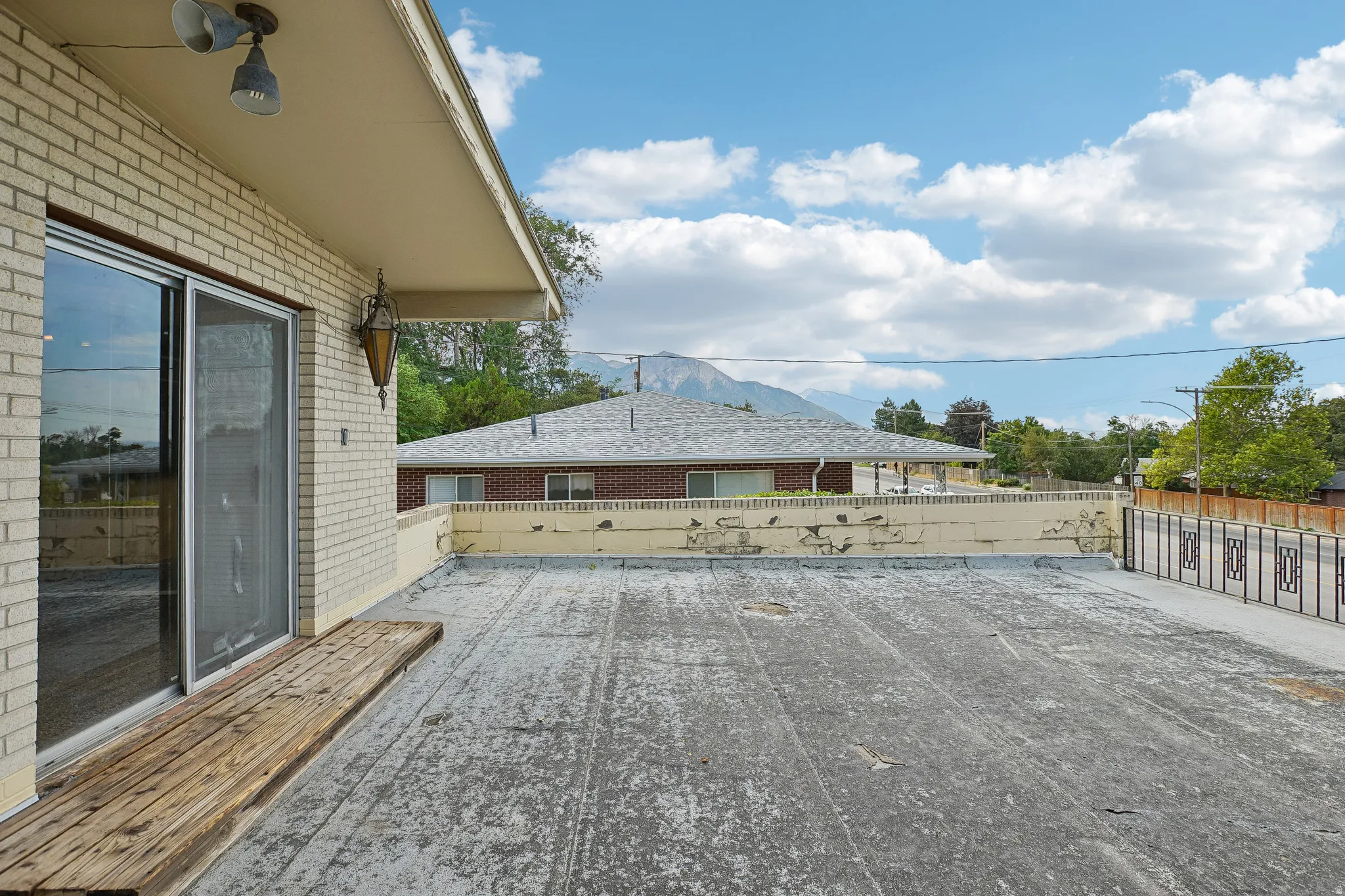 Sliding glass door access, exterior brick facade, outdoor wall-mounted light fixture, and distant mountain backdrop