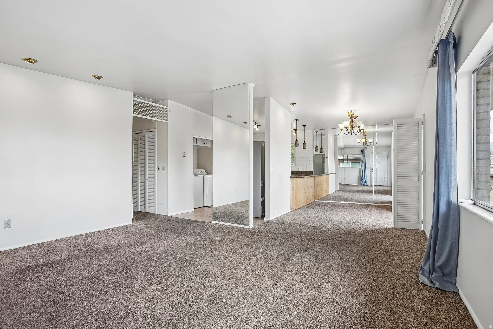 Recessed ceiling lighting, mirrored accent wall, wood-finish kitchen peninsula, contemporary pendant lighting, and a chandelier in the dining area