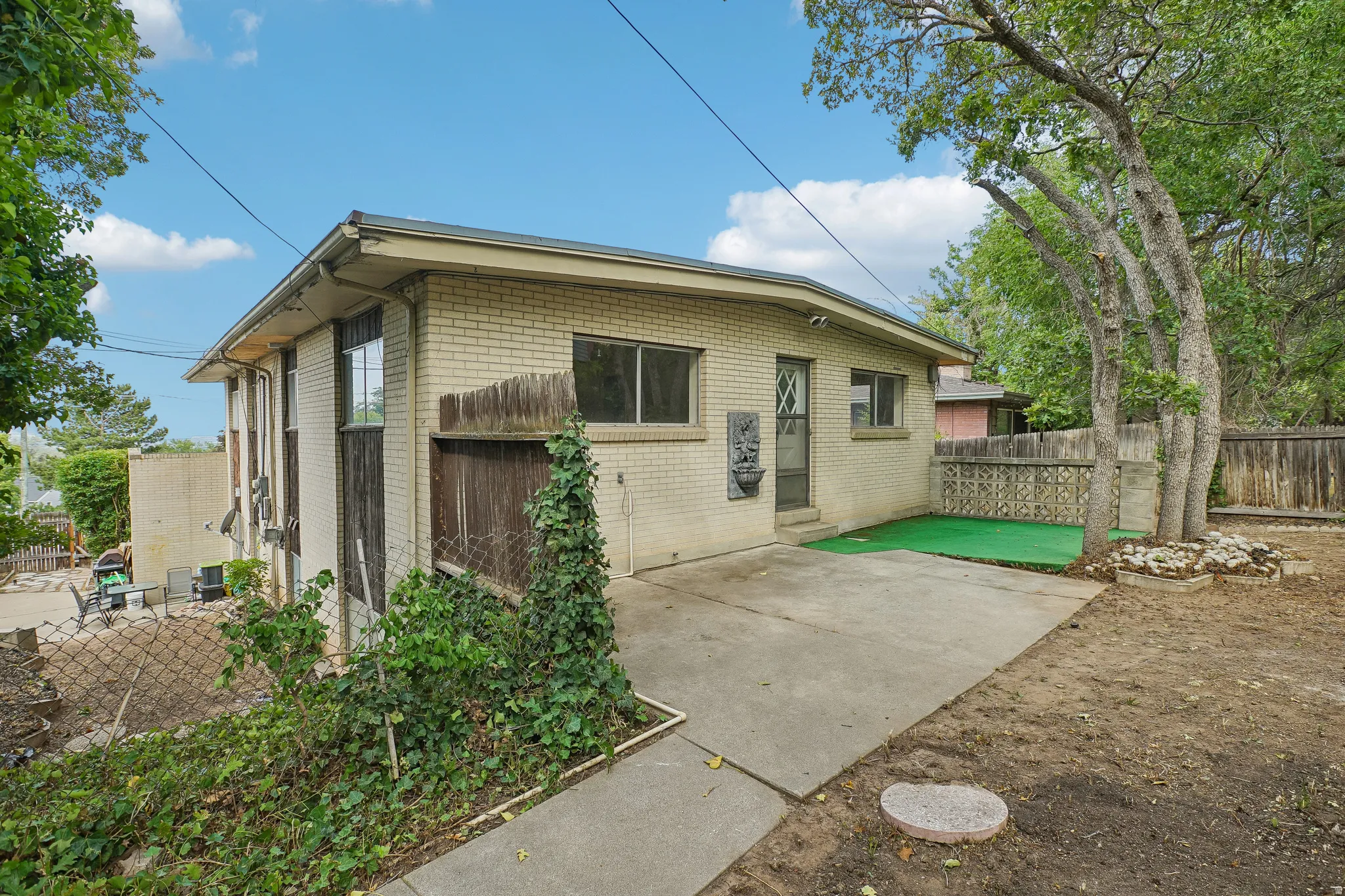 Brick exterior with multiple windows, concrete patio, and a sloped, treed yard