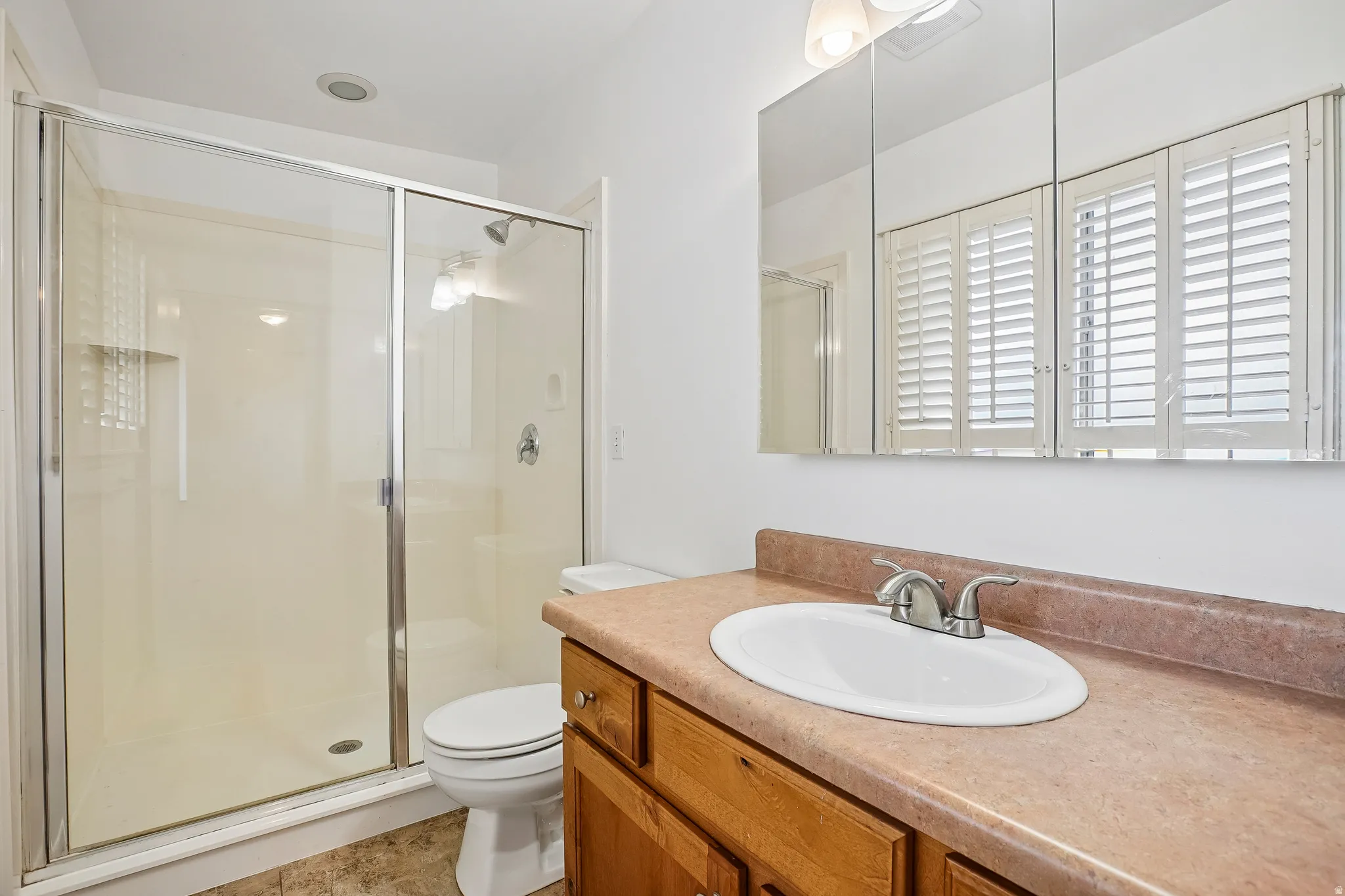Glass-enclosed shower with integrated shelving, single vanity with oval sink, brushed nickel faucet, and a wall-mounted medicine cabinet with mirror panels