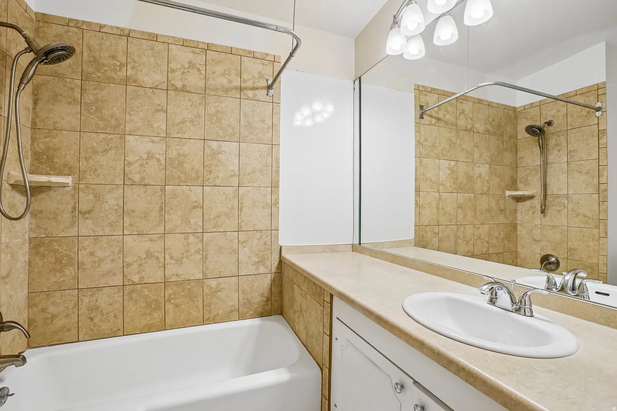 Tub and shower combination with tiled surround, single vanity with integrated sink, and overhead lighting fixture