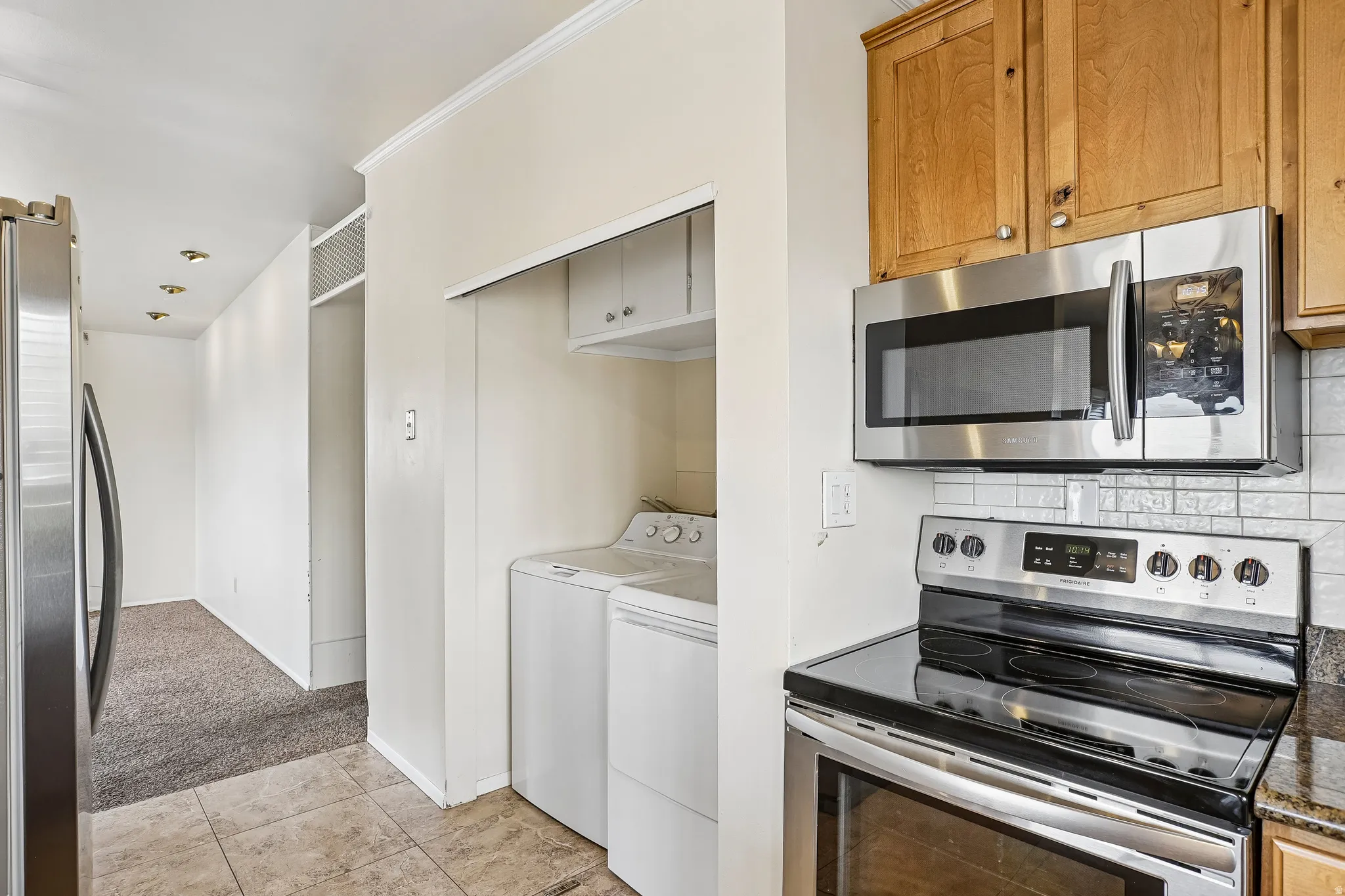 Stainless steel appliances, wood-finish cabinetry, tile flooring, laundry area, and recessed lighting