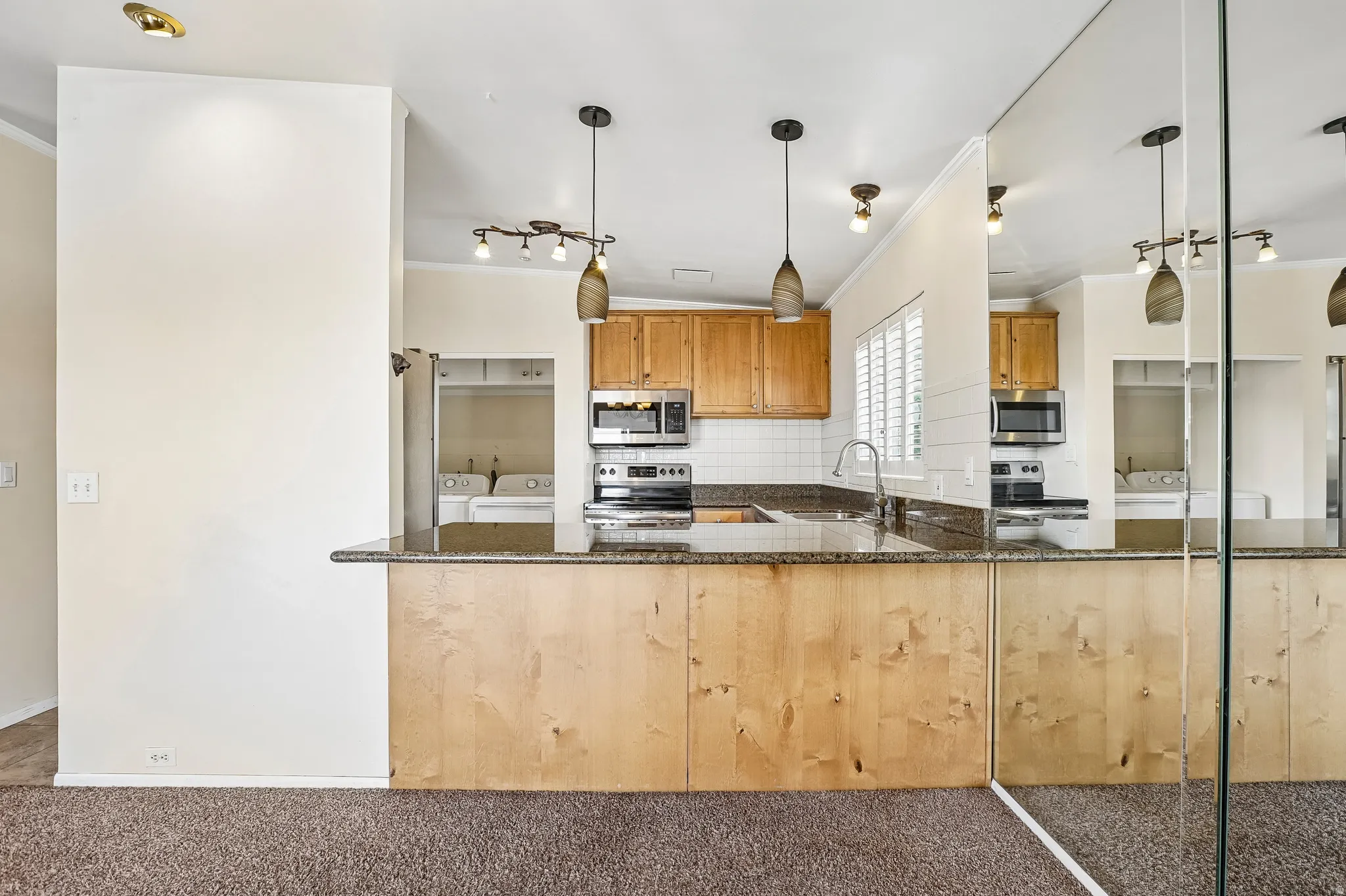 Kitchen with granite-look countertops, light wood cabinetry, stainless steel appliances, and pendant lighting