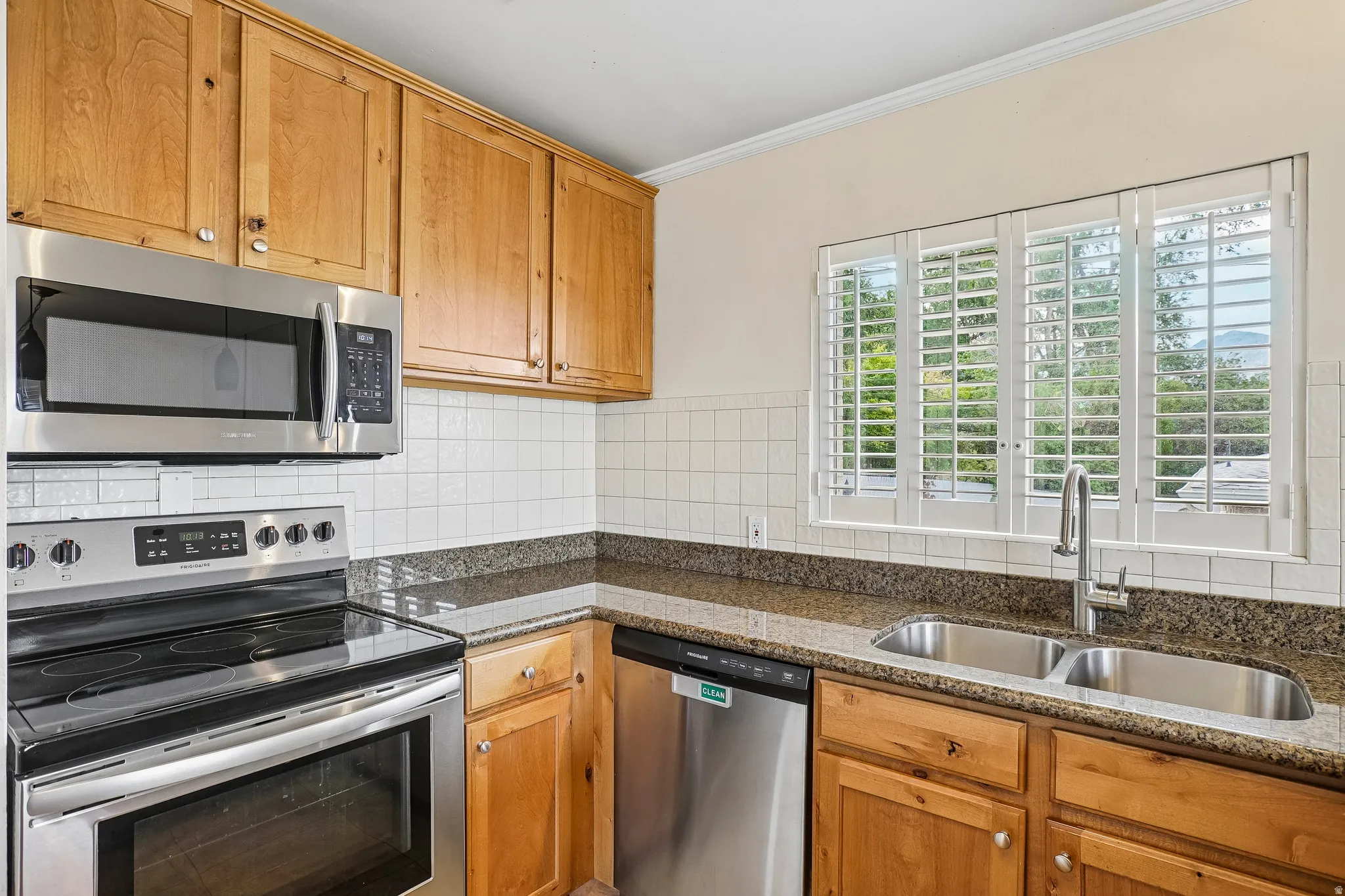 Kitchen featuring wood cabinetry, stainless steel appliances, speckled countertops, a tile backsplash, and a double basin sink