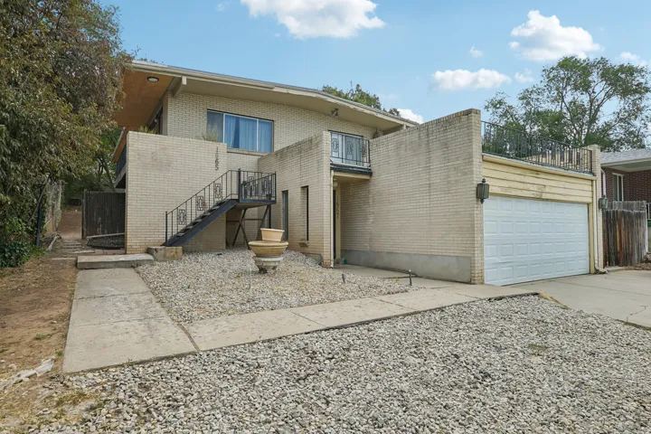 Brick exterior with a two-car garage, wrought iron staircase, and a low-maintenance gravel and concrete front yard