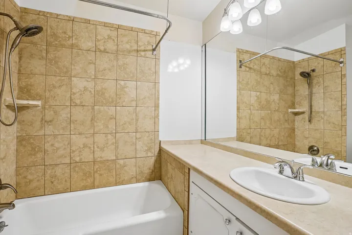 Tub and shower combination with tiled surround, single vanity with integrated sink, and overhead lighting fixture