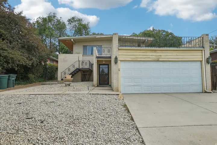 Two-car garage with a paneled door, exterior brick siding, and a partial upper balcony with metal railing