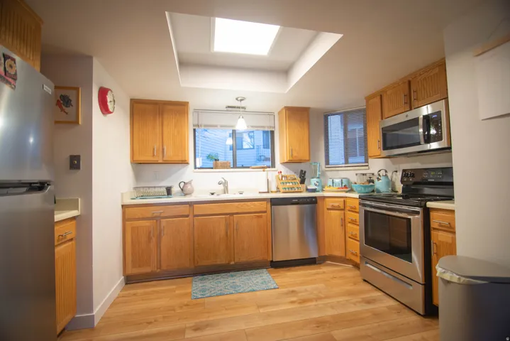 Kitchen featuring wood-finish flooring, recessed lighting, wood cabinetry, stainless steel appliances, and a skylight