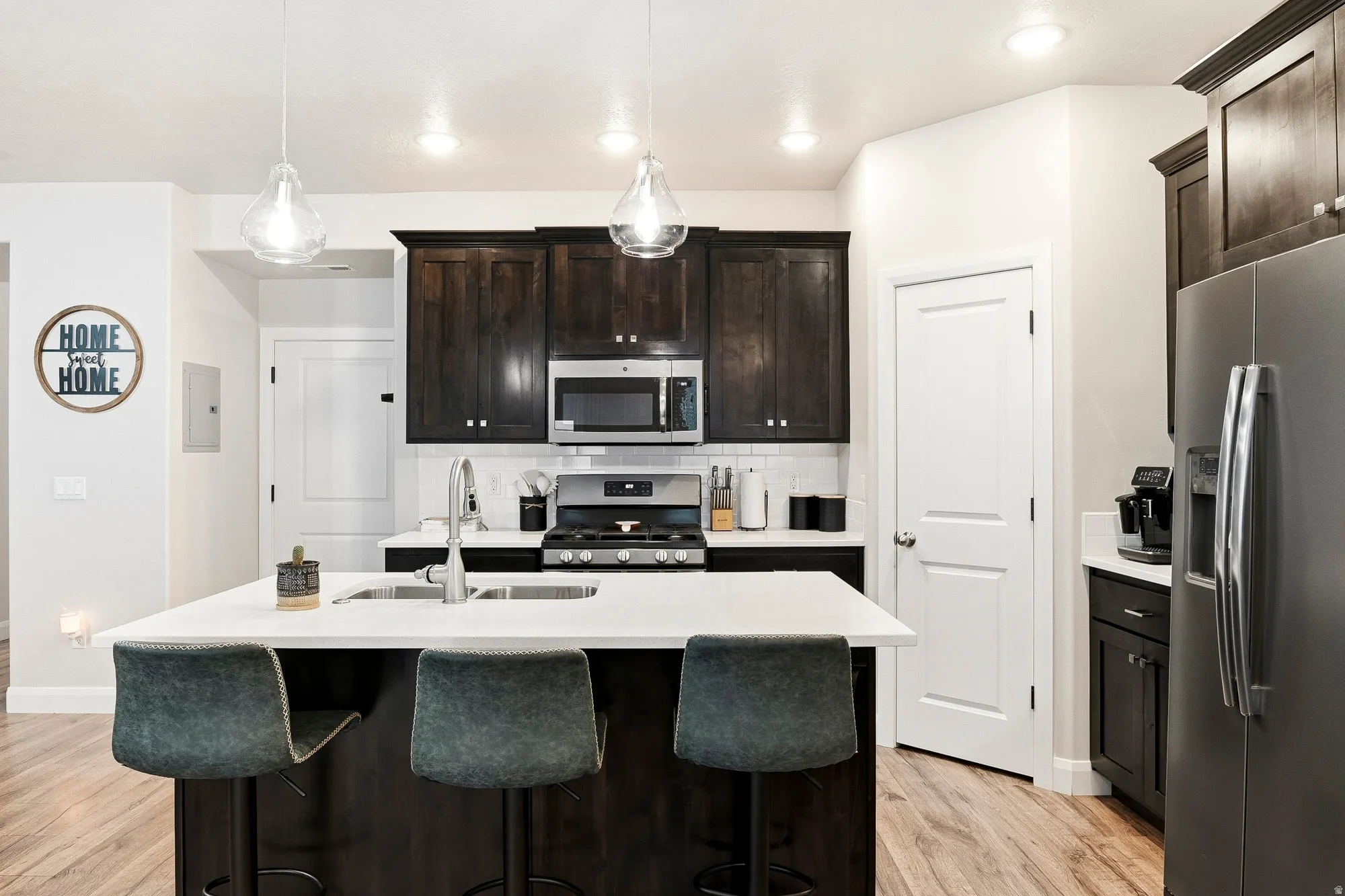 Kitchen featuring a central island with an integrated sink, dark wood-finish cabinetry, stainless steel appliances, and light-colored countertops