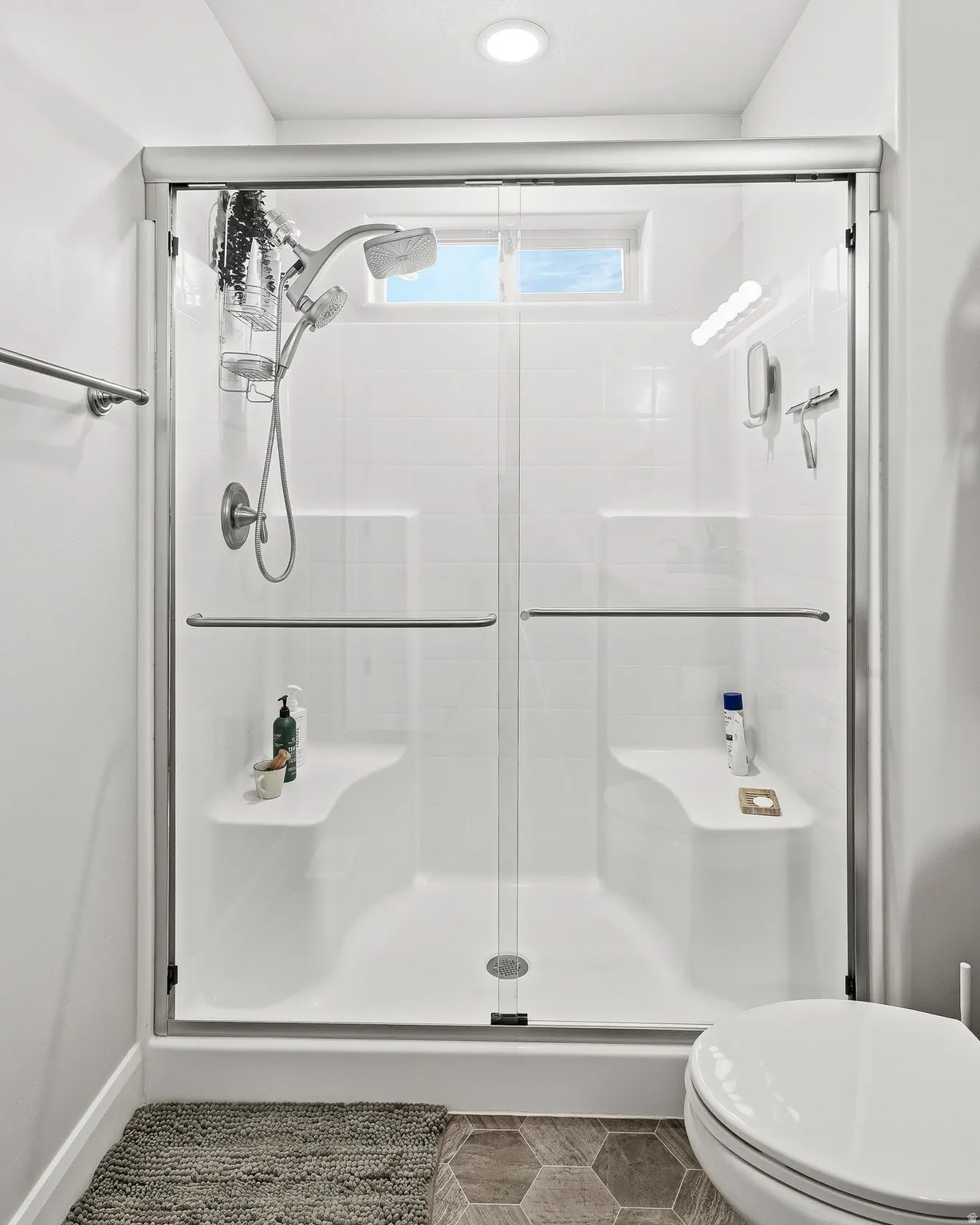 White tiled shower stall with sliding glass doors, built-in benches, and a small transom window