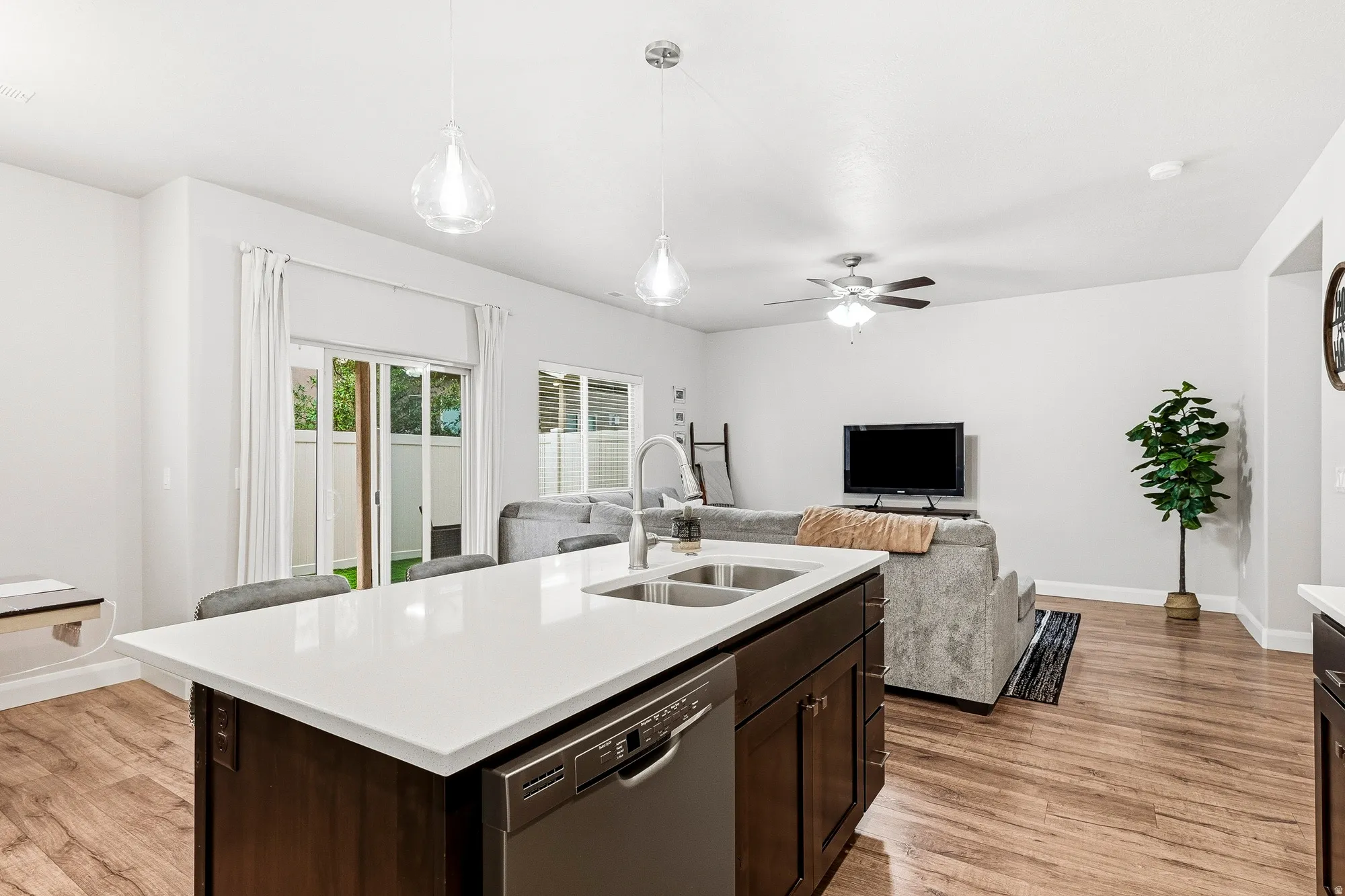 Open-concept living space featuring wood-finish flooring, a kitchen island with a double basin sink, and pendant lighting