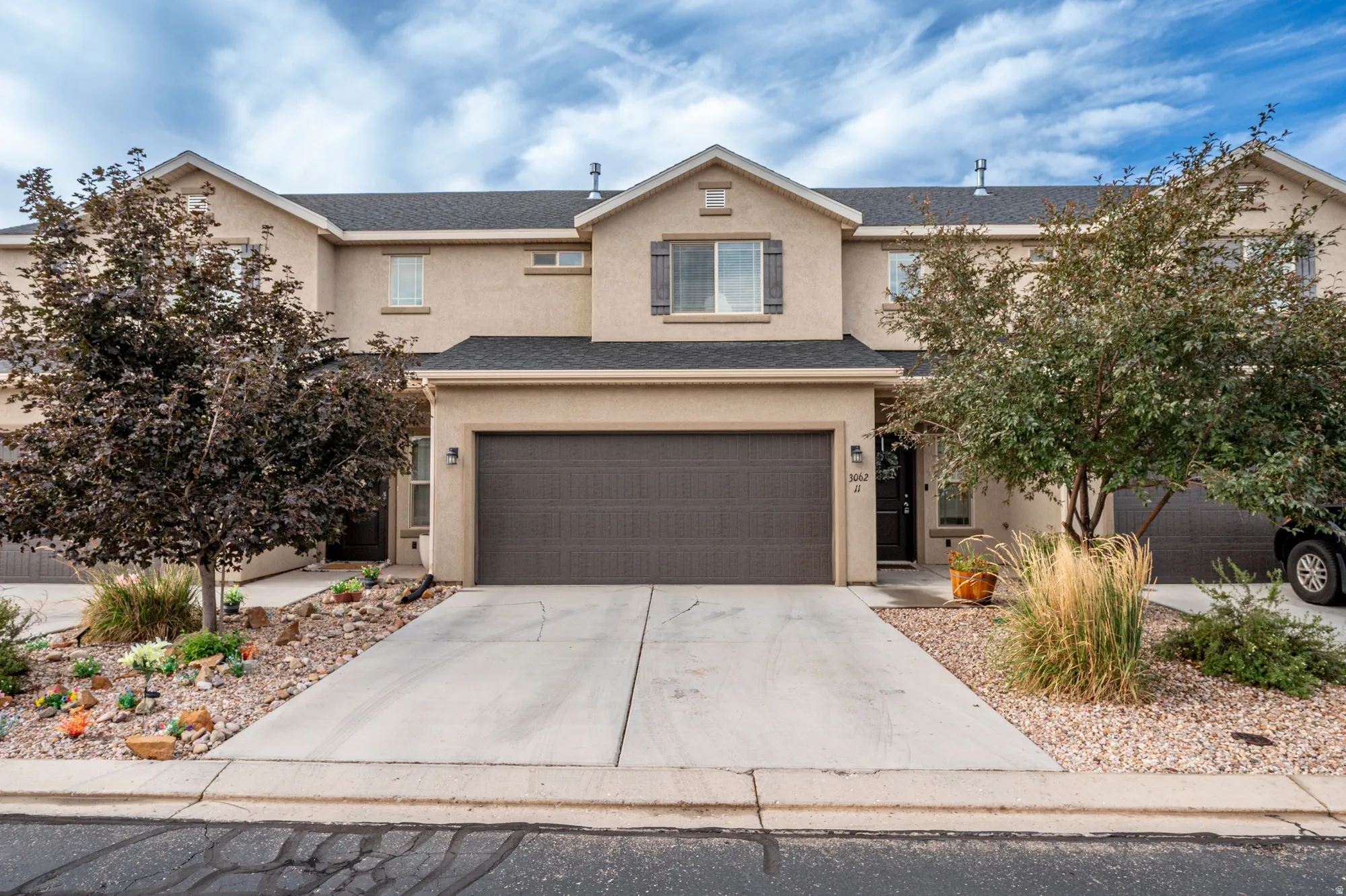 Stucco exterior with an attached garage, paved driveway, and mature landscaping