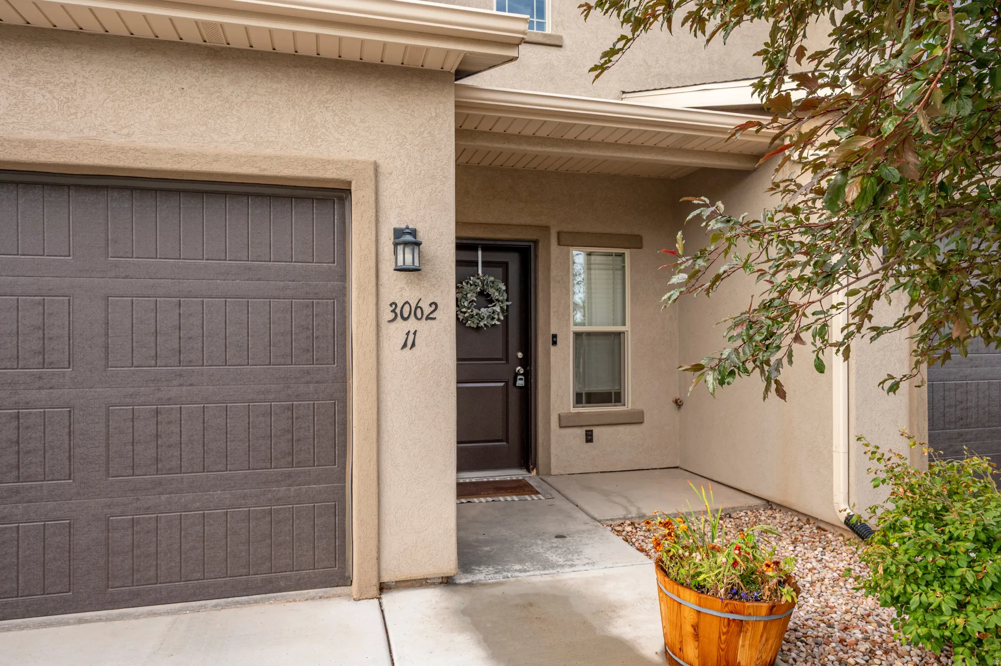 Attached garage with panel detailing, stucco exterior, exterior wall lantern, and front entry door