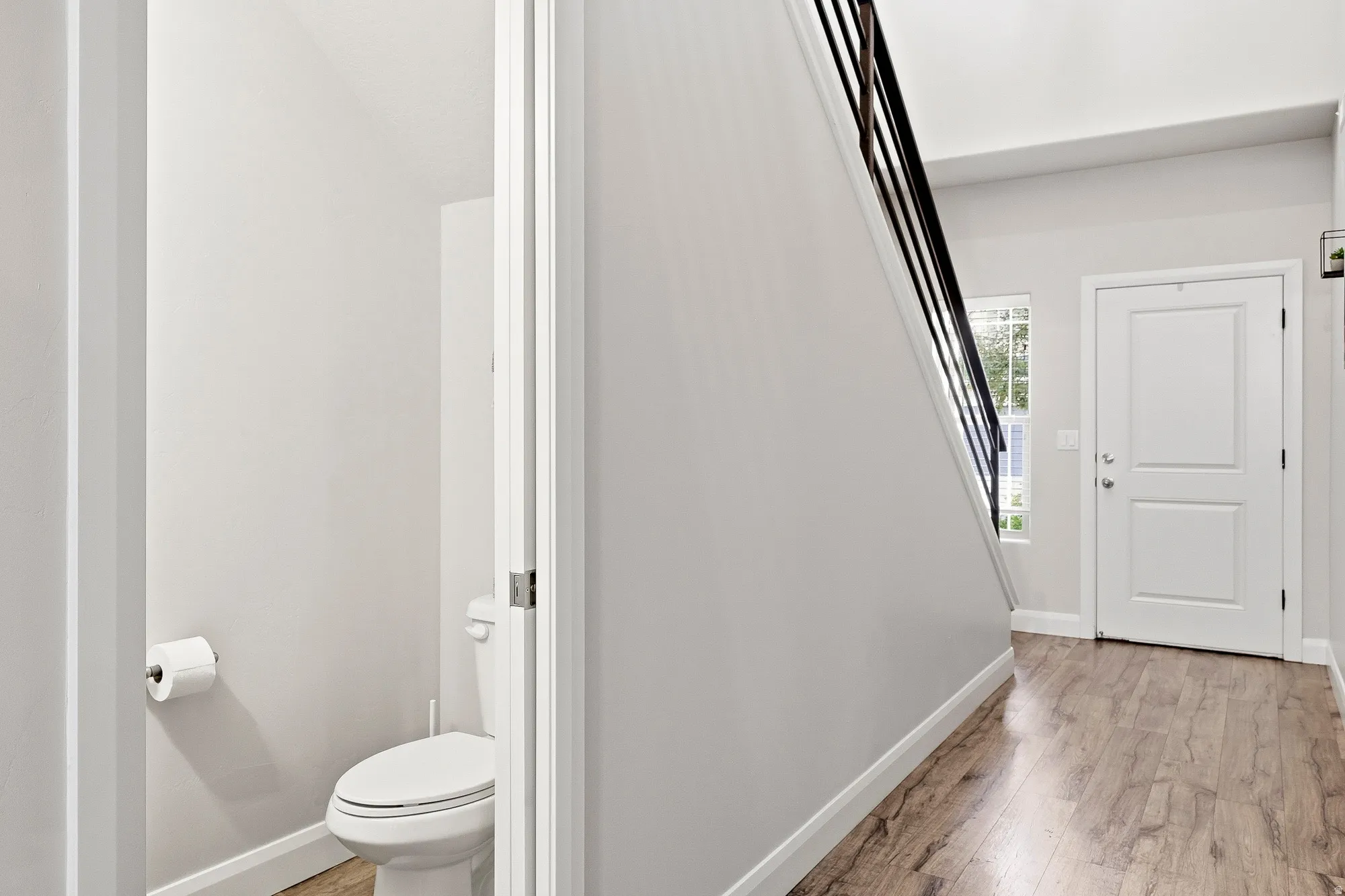 Wood-finish flooring, white paneled interior door, and black metal stair railing