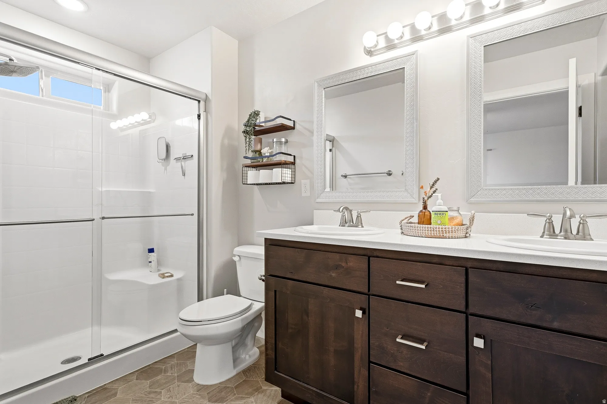 Dual vanity with white countertops, wood-finish cabinetry, and two framed mirrors