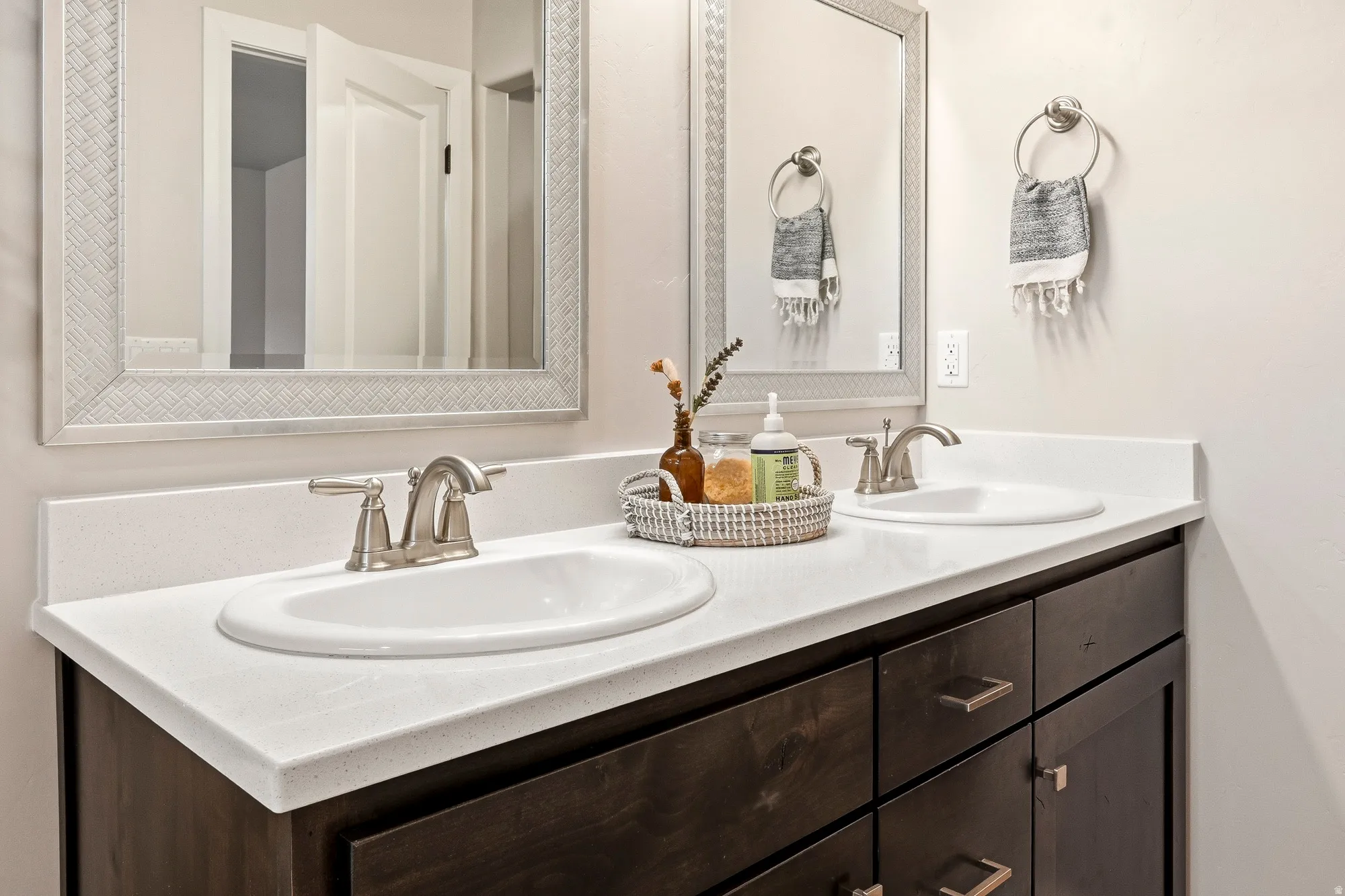 Dual undermount sinks with brushed nickel faucets, solid surface vanity countertop, and dark wood-finish cabinetry