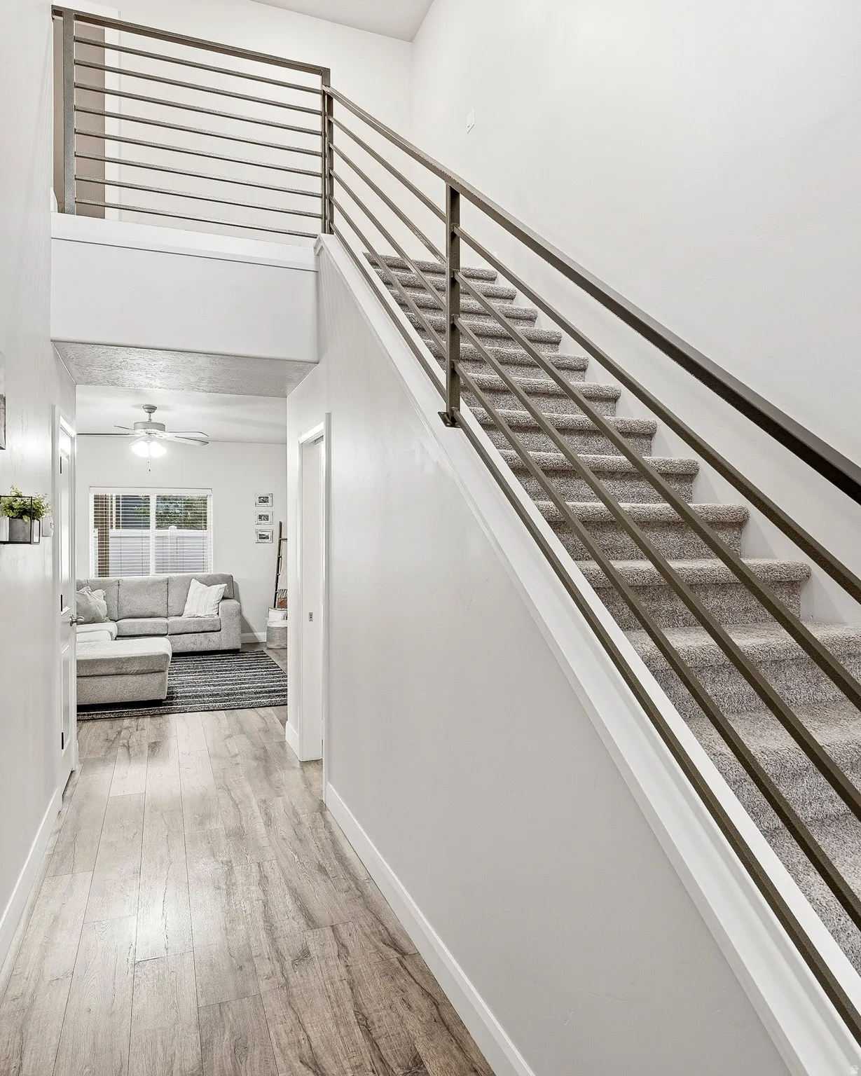 Open-concept living area with wood-finish flooring, a carpeted staircase, and contemporary metal railings
