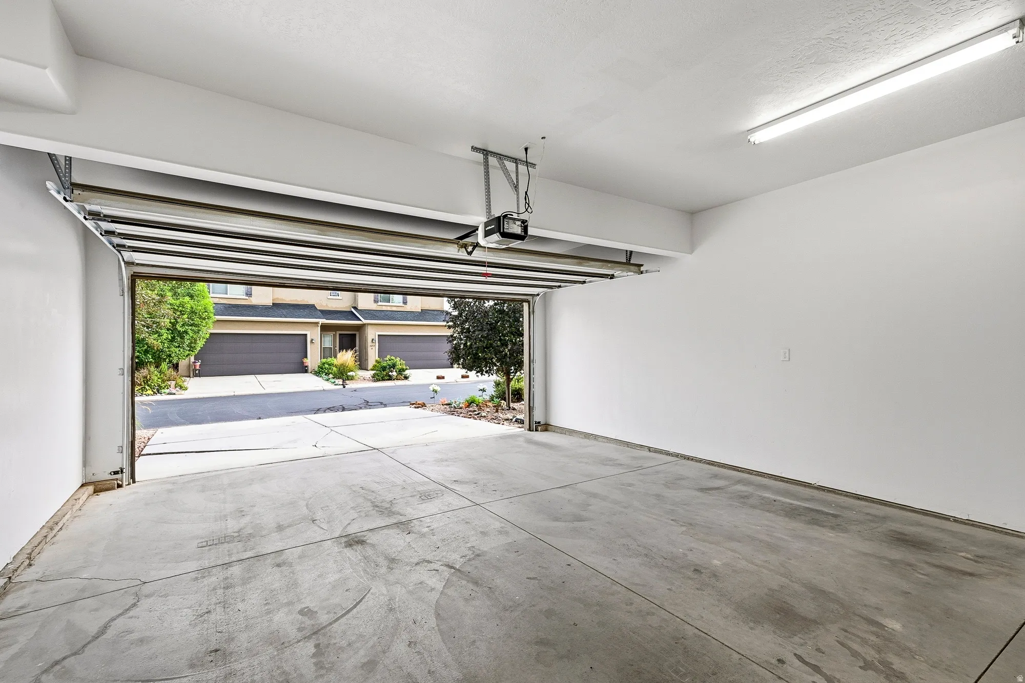 Spacious garage with concrete flooring, automatic garage door opener, and overhead fluorescent lighting