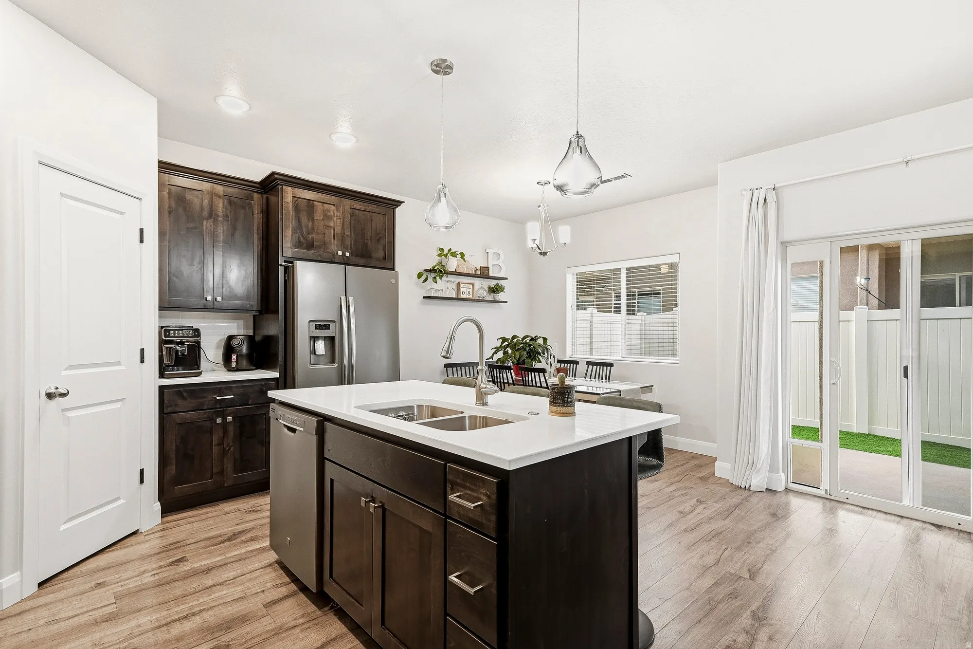 Modern kitchen featuring dark wood cabinetry, stainless steel appliances, a center island with sink, wood-finish flooring, and sliding glass doors to the exterior
